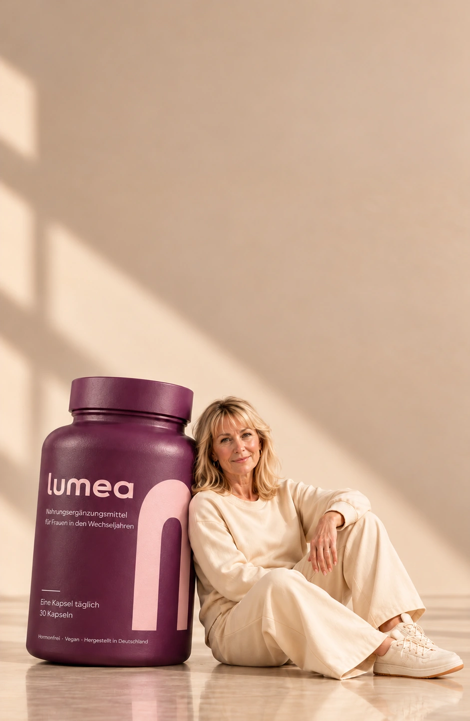 Eine Frau in cremefarbenem Outfit neben einer tiefpflaumenfarbenen Lumea-Flasche im warmen Sonnenlicht.